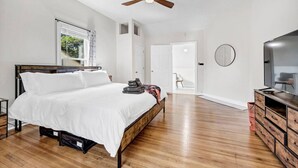Une chambre à coucher avec un lit, un ventilateur de plafond, une télévision et une commode en bois.