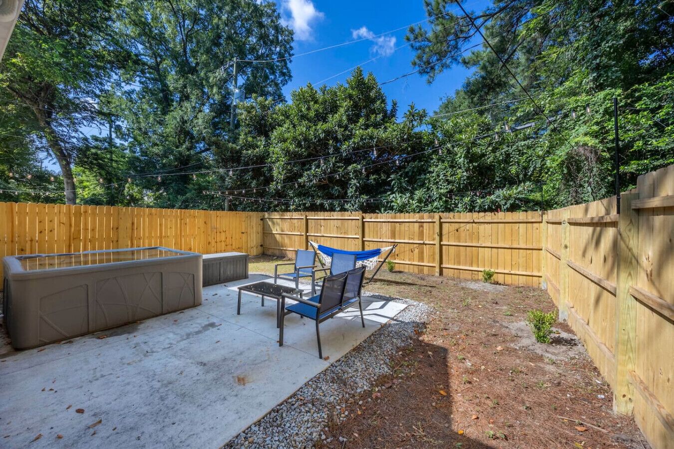 Un patio trasero con un patio de hormigón, una barbacoa integrada y una valla de madera.