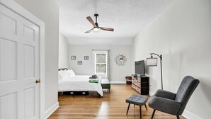 Un dormitorio con cama, una silla, un mueble para televisor y un ventilador de techo.