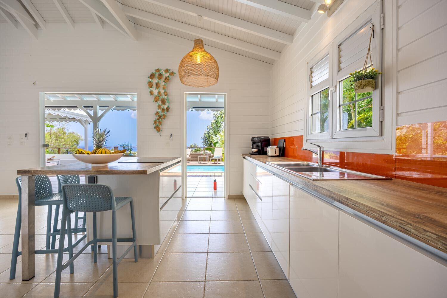 A modern kitchen with a large island, bar stools, a hanging light fixture, and a view of the outdoors.
