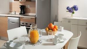A modern kitchen with a refrigerator, a coffee maker, and a dining table set with cups and a fruit basket. - Cozy Cottage in Queven for 6 (Queven)