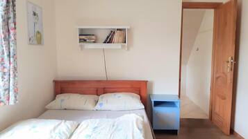 Un dormitorio con cama, mesita de noche, armario y una estantería con libros.