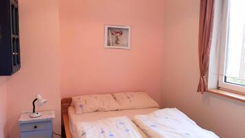 A bedroom with a bed, a nightstand, a lamp, a framed picture, and a window with curtains.