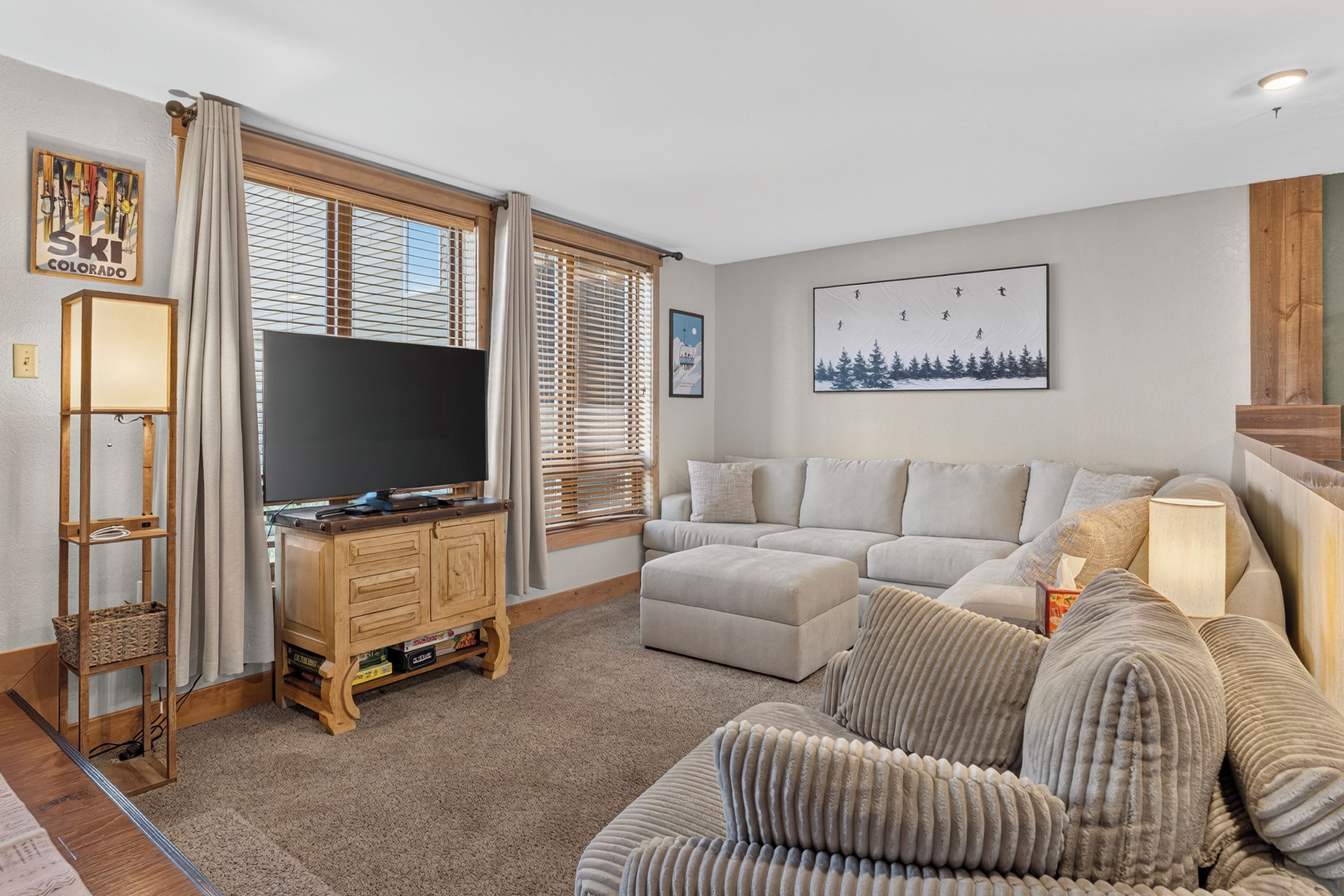 A living room with a flat-screen TV on a wooden stand, a grey sofa, and a patterned armchair.