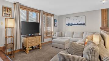 A living room with a flat-screen TV on a wooden stand, a grey sofa, and a patterned armchair.