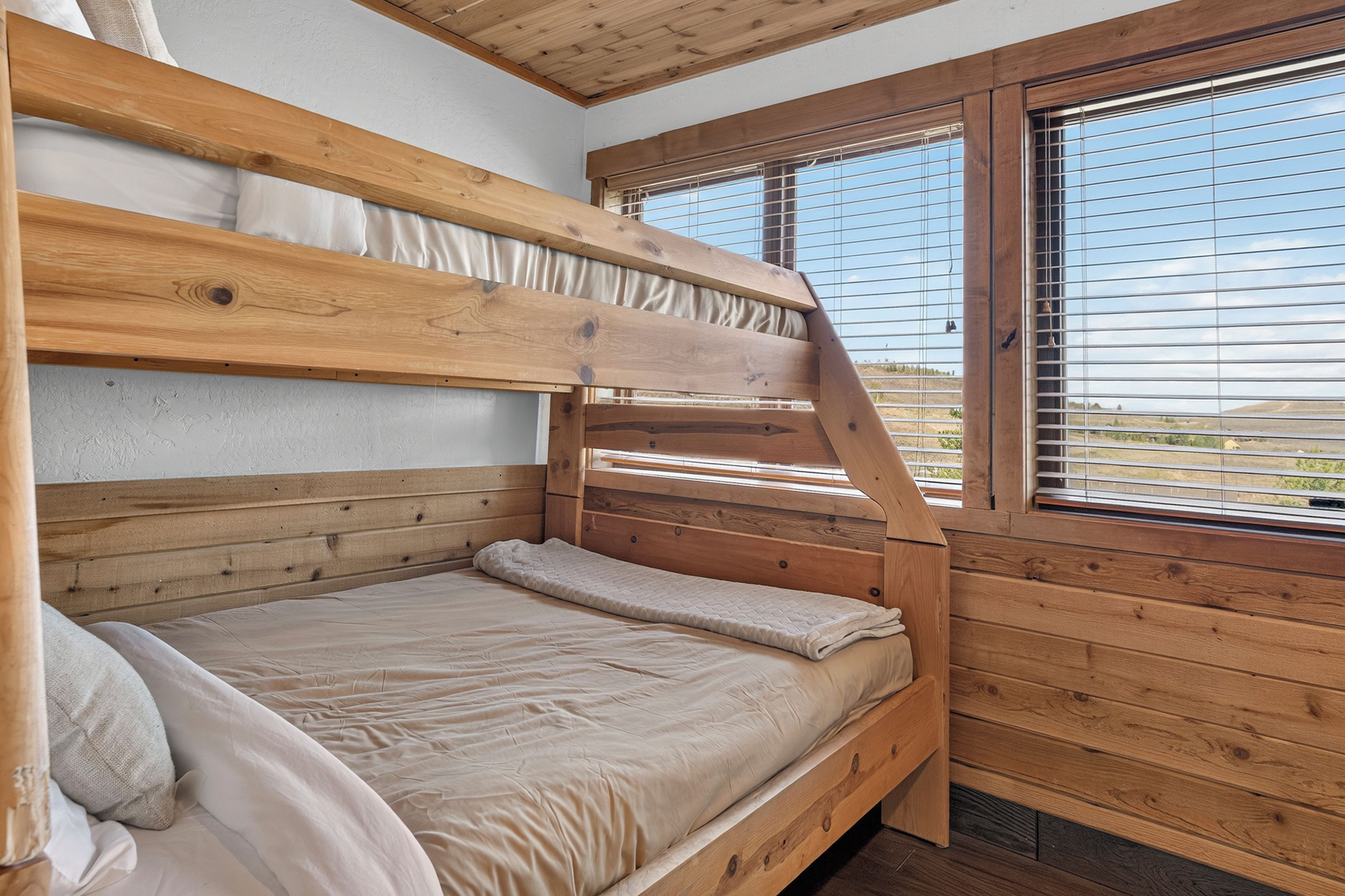 A bunk bed with a wooden headboard and a window with blinds.
