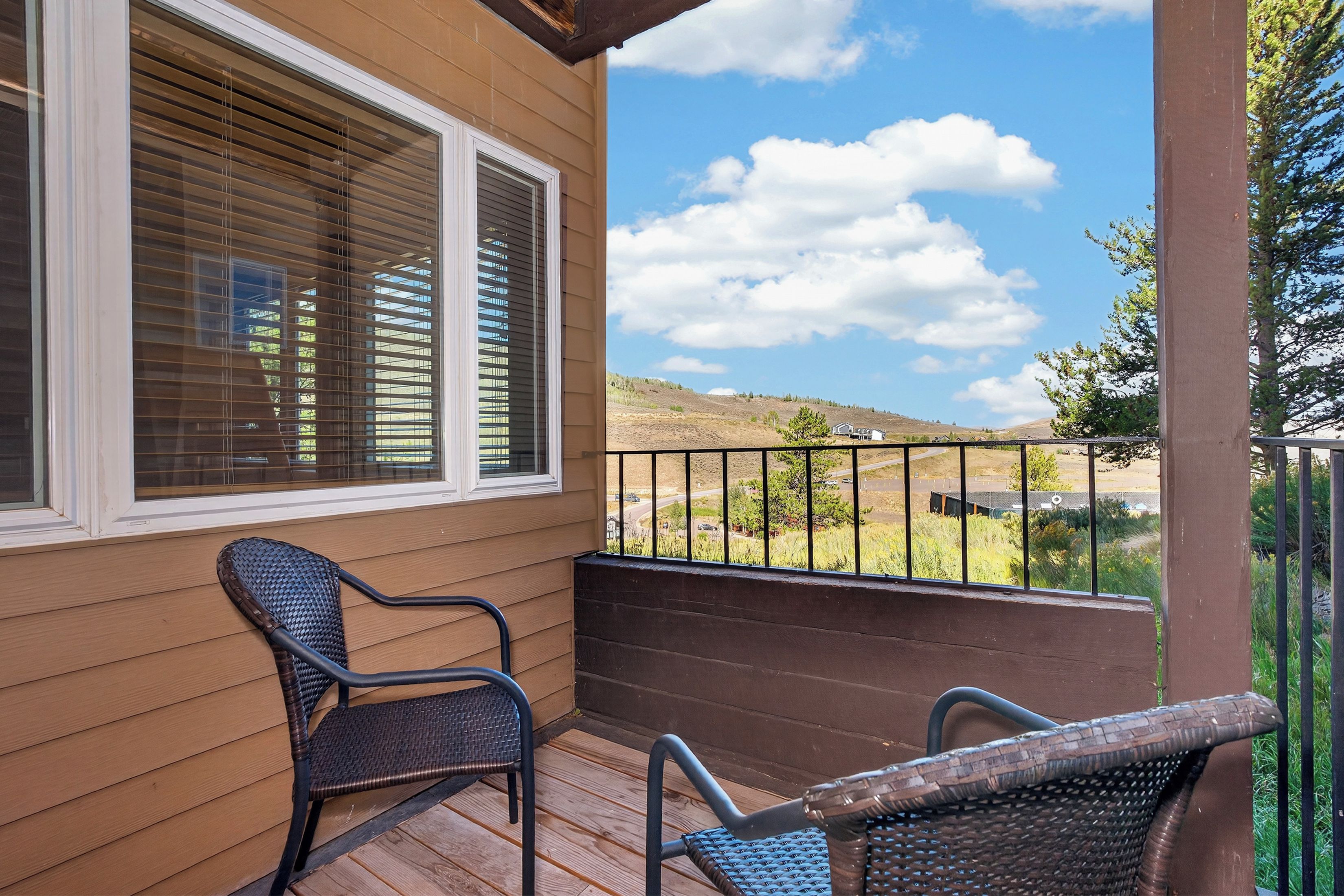 A wooden deck with two wicker chairs and a view of a hilly landscape.