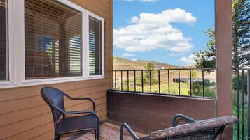 A wooden deck with two wicker chairs and a view of a hilly landscape.