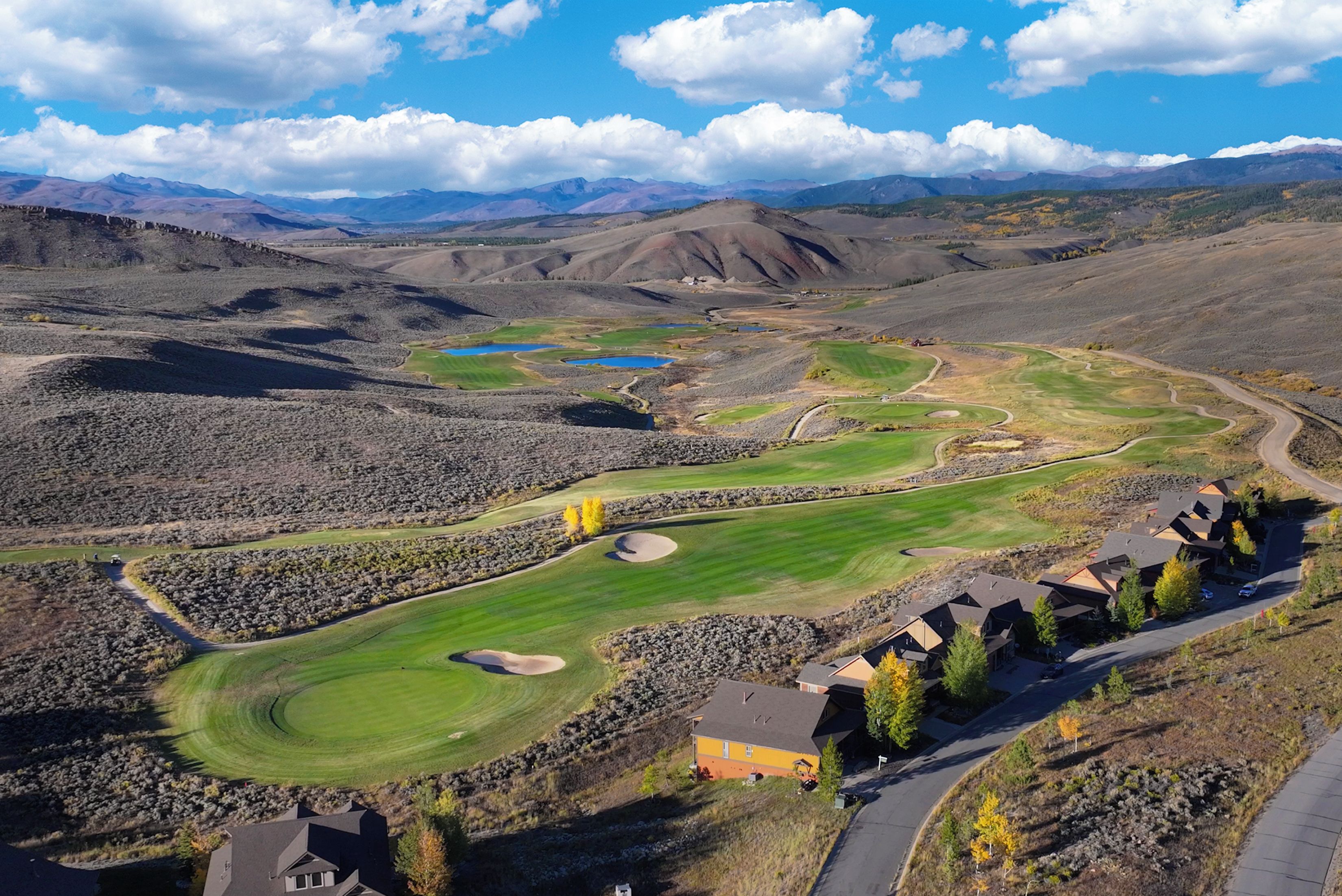 A golf course with bunkers, a pond, and a residential area with houses.