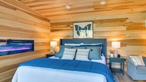 A room with a bed, two bedside tables, a wall-mounted TV, and a wooden ceiling. - Waterfront cabin-Couples getaway *Private hot tub* (Cherokee)
