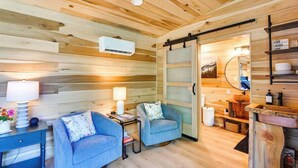A cozy cabin interior with wooden walls, a sofa, a small table with a lamp, and a bathroom with a mirror and shelves. - Waterfront cabin-Couples getaway *Private hot tub* (Cherokee)