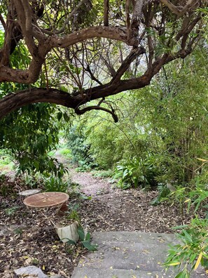 Ein Garten mit einem Kiesweg, einem Metalltisch und einem großen Baum.