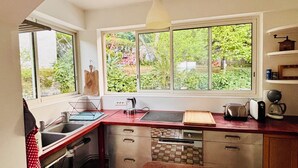 A kitchen with a sink, stove, and large windows offering a view of greenery. - Family home sleeps 12, lush garden, sea view. Close to beaches. (Roquebrune-Cap-Martin)