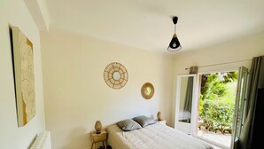 A bedroom with a bed, a radiator, a bedside table with a lamp, and a window with a view of greenery. - Family home sleeps 12, lush garden, sea view. Close to beaches. (Roquebrune-Cap-Martin)