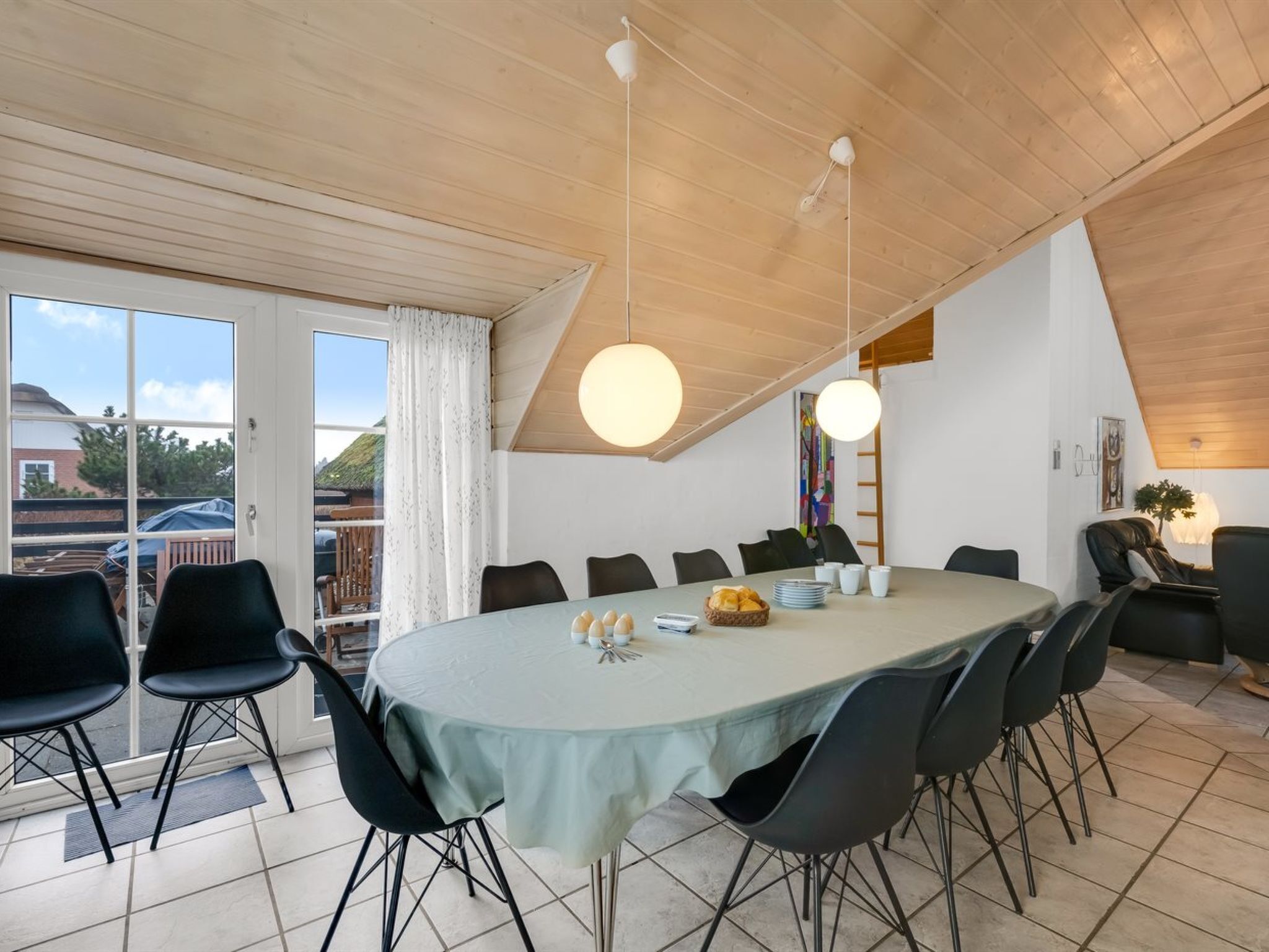 Un espace repas avec une grande table ovale, des chaises noires et des luminaires suspendus.