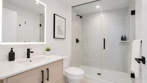 A modern bathroom with a white sink, black faucet, and a glass-enclosed shower.