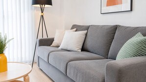A grey sofa with multiple cushions, a round wooden coffee table, a floor lamp, and a framed picture on the wall.