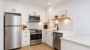 A modern kitchen with stainless steel appliances, white cabinetry, and a wooden countertop.