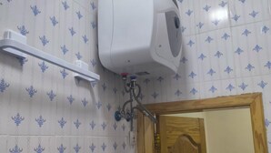 A bathroom with patterned tiles, a white wall-mounted air conditioning unit, a wooden door, and a white shelf.