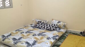 A bedroom with a bed, a window with a metal grille, a bedside table, and a rug.