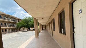 A covered walkway with a tiled floor, a white door with a no smoking sign, and a building with multiple windows and balconies. - Hotel los Pinos (Cadereyta Jiménez)