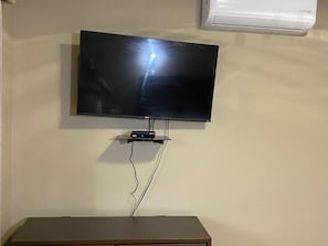 Seinälle asennettu litteänäyttöinen televisio, johon on kytketty kaapeli alla olevassa laitteessa.