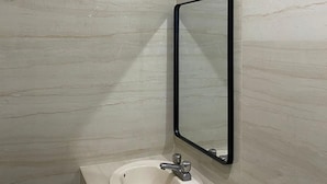 A bathroom with a marble wall, a sink with a single faucet, and a mirror with a black frame. - Hotel los Pinos (Cadereyta Jiménez)