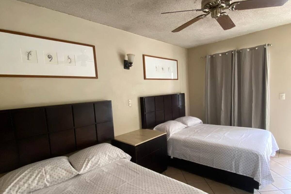 Ein Hotelzimmer mit zwei Betten, einem Deckenventilator und gerahmten Bildern an der Wand.