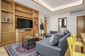 Ein modernes Wohnzimmer mit Fernseher, Sofa, Couchtisch und Holzregalen.