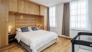 Un dormitorio con cama, armarios de madera, mesita de noche, lámpara y ventana con cortinas.