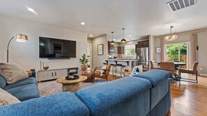 A modern living room with a TV, sofa, coffee table, and dining area with chairs and a table.