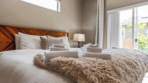 Una cama bien hecha con un edredón mullido y toallas enrolladas, un cabecero de madera, una lámpara y vistas a la vegetación.