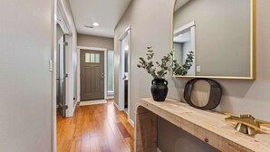 Un couloir avec un plancher en bois, une porte, un miroir et une plante en pot.