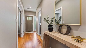 A hallway with wooden flooring, a door, a mirror, and a potted plant.