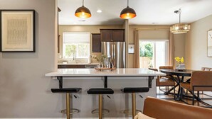 Une cuisine moderne dotée d’un îlot central, de tabourets de bar et de luminaires suspendus.