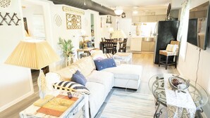 A living room with a sofa, coffee table, and lamp. There is a dining area with chairs and a table. A kitchen is visible in the background. - Lovely 2-bedroom house with AC in charming Chipley. (Chipley)