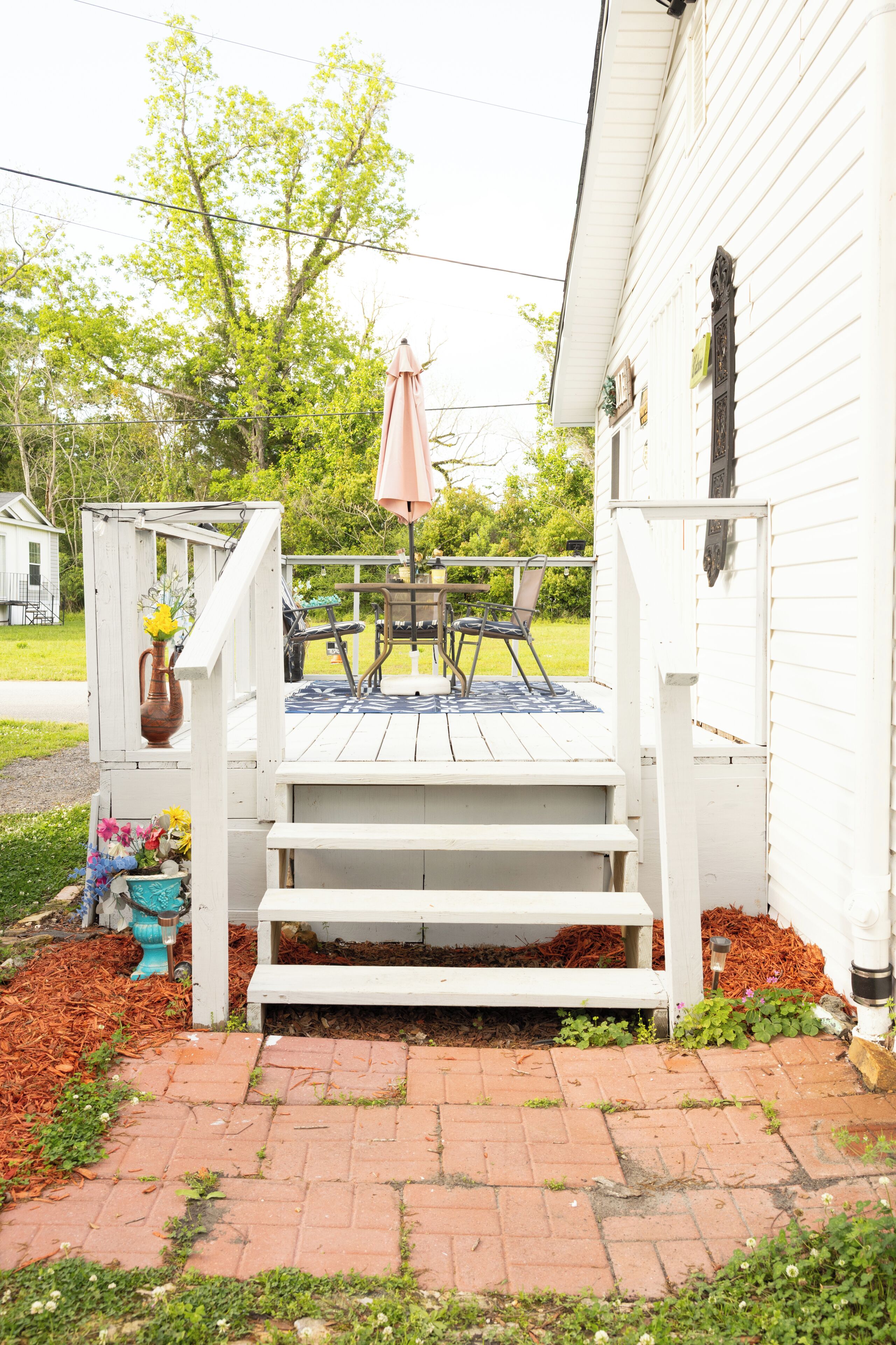 A wooden deck with a table and chairs, a potted plant, and a small garden area with mulch and plants.