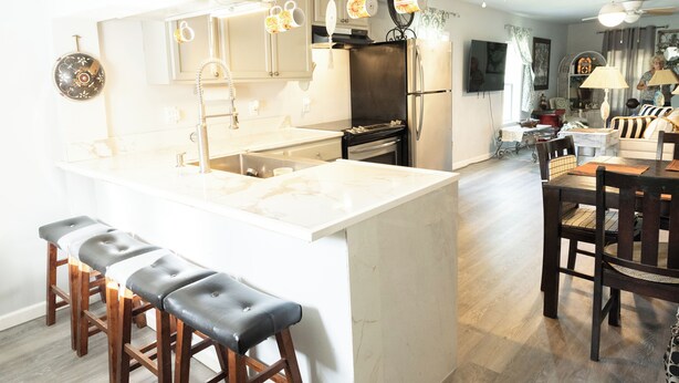 A modern kitchen with a central island, bar stools, and a dining area with a table and chairs. - Lovely 2-bedroom house with AC in charming Chipley. (Chipley)