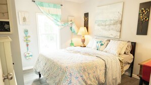 A bedroom with a bed, a nightstand, a lamp, a window with curtains, and a wall with a painting. - Lovely 2-bedroom house with AC in charming Chipley. (Chipley)