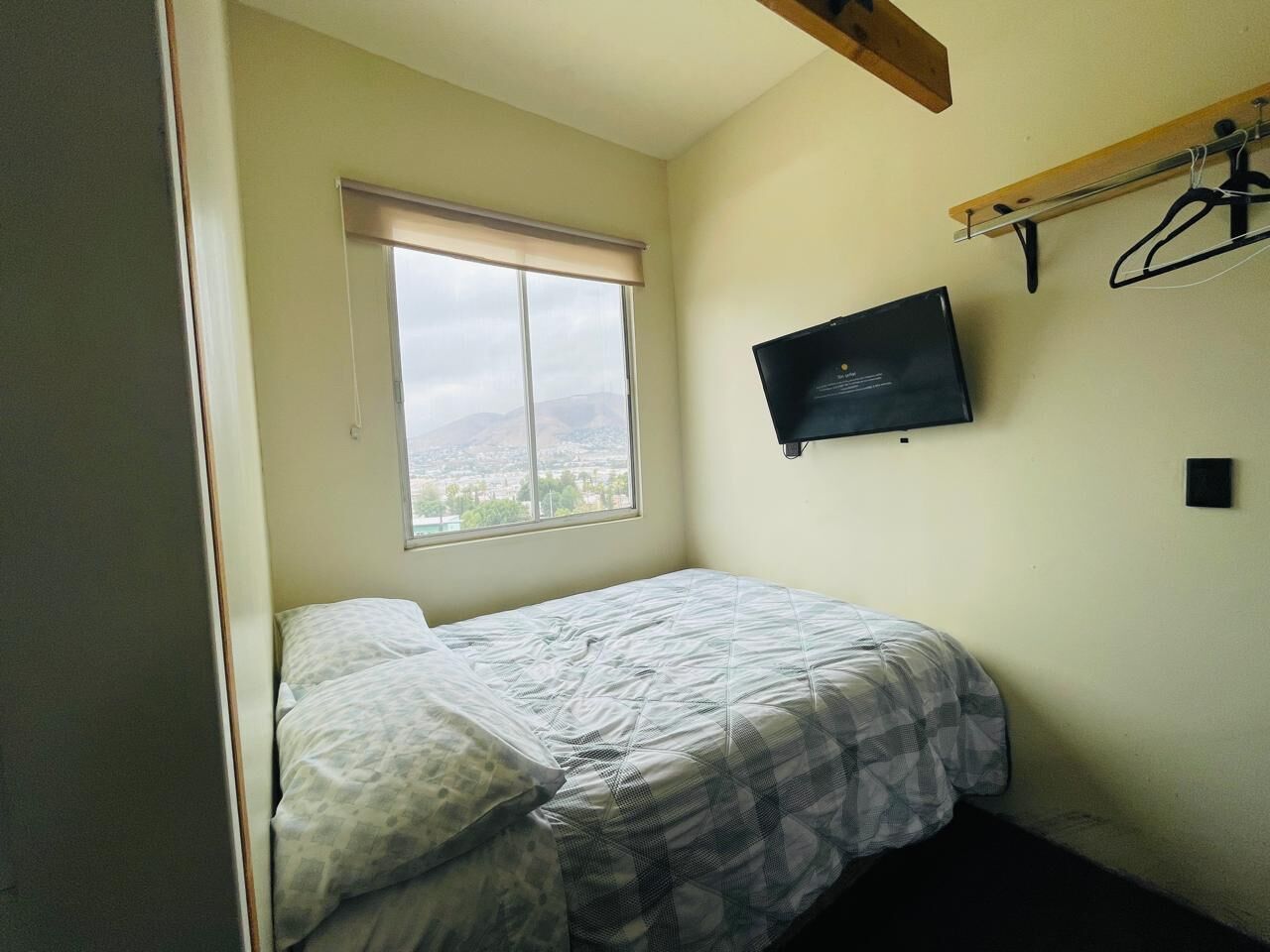 A bedroom with a bed, a window with a view, a mounted TV, and a coat rack.