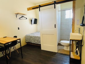 A small room with a bed, a desk, a chair, a TV, a bathroom with a toilet and sink. - Estudios Pinos (Tijuana)