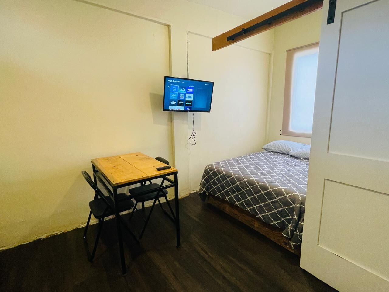 Una habitación pequeña con una cama, un escritorio y un televisor montado en la pared.