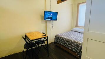 Una habitación pequeña con una cama, un escritorio y un televisor montado en la pared.