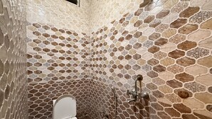 Une salle de bain avec un mur décoré d’une mosaïque de pierre, des toilettes et une douche.