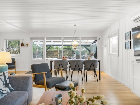 A modern living room with a dining area, wooden floors, and large windows.