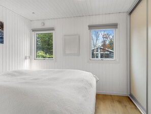 A bedroom with a bed, two windows, and a view of trees and a building.