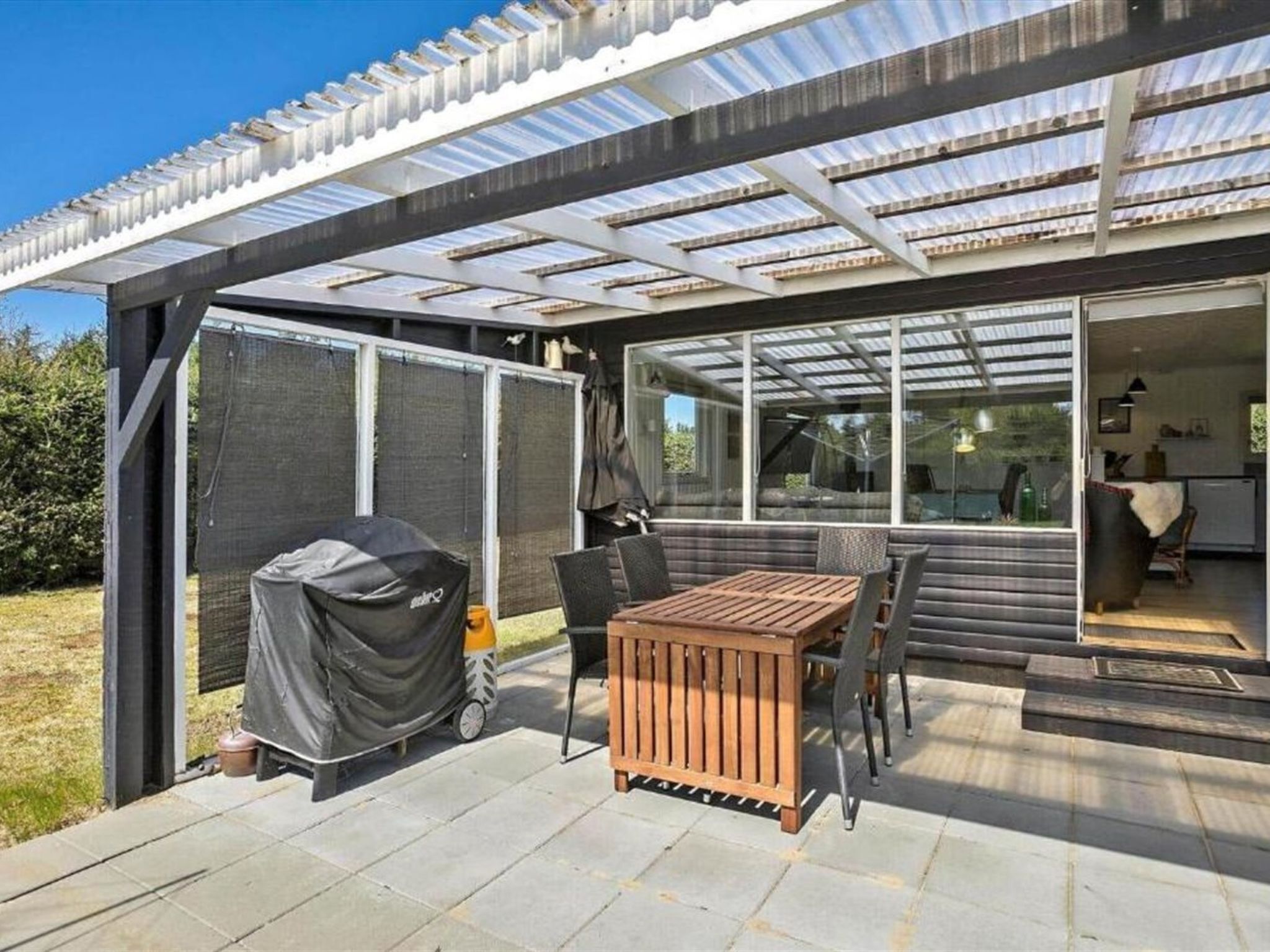A covered patio with a table and chairs, a grill, and a sliding glass door leading to an interior space.