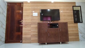 A room with a wooden door, a TV mounted on a wooden panel wall, and a cabinet with drawers. - SS Paradise Residency (Tiruvannamalai)
