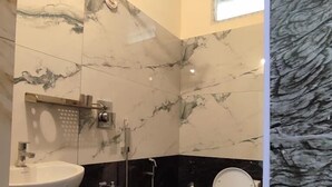 A bathroom with a sink, toilet, shower, and marble walls. - SS Paradise Residency (Tiruvannamalai)