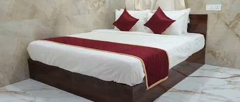 Un lit avec une couvre-lit blanche et rouge, deux oreillers rouges et une tête de lit en bois foncé.